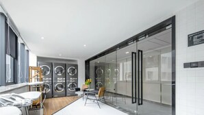 A modern laundry room with built-in washers and dryers, a small seating area with chairs, and a large window providing natural light.