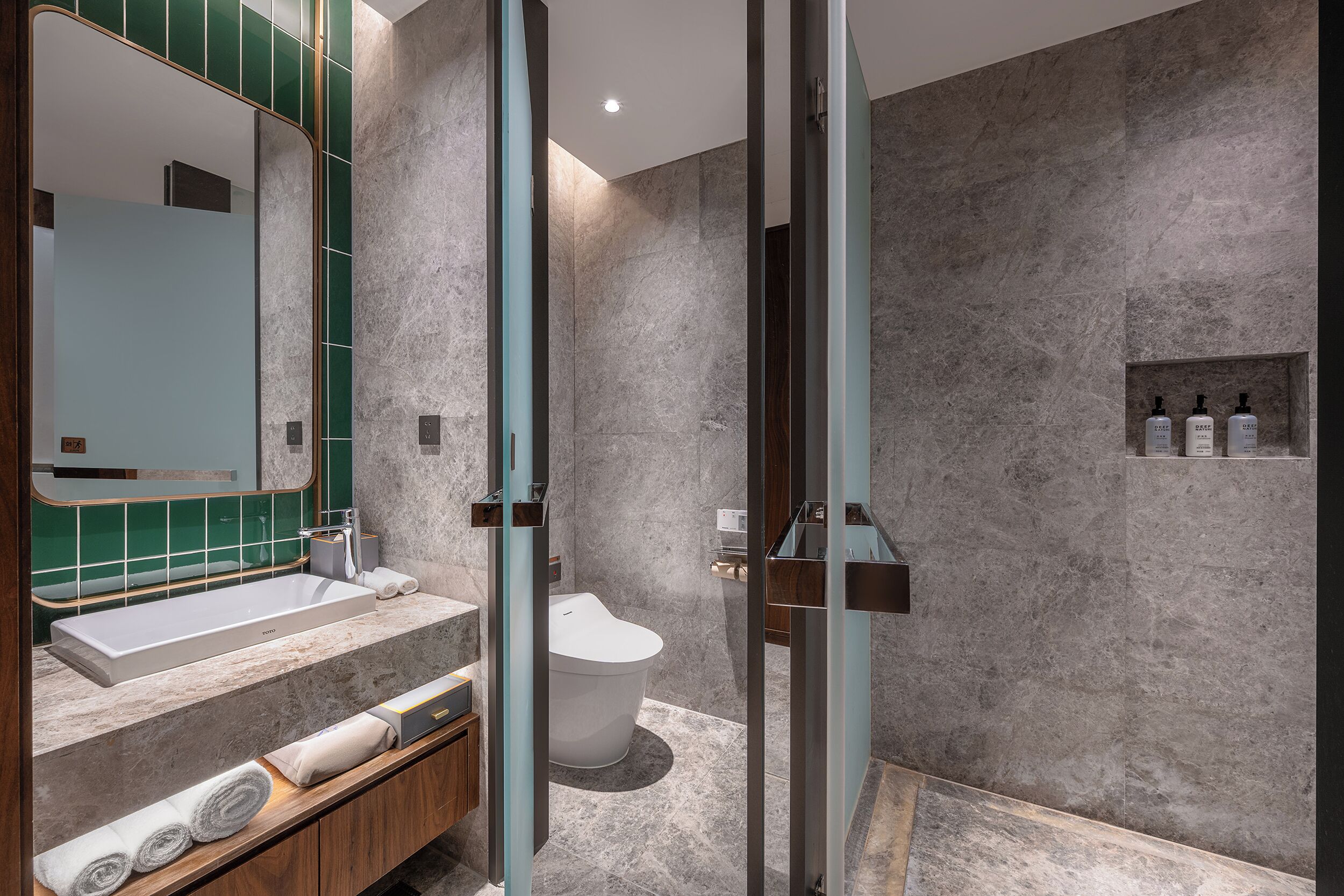 A modern bathroom with a large mirror, a built-in sink, and a toilet. There are towels and toiletries on the counter.