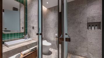 A modern bathroom with a large mirror, a built-in sink, and a toilet. There are towels and toiletries on the counter.