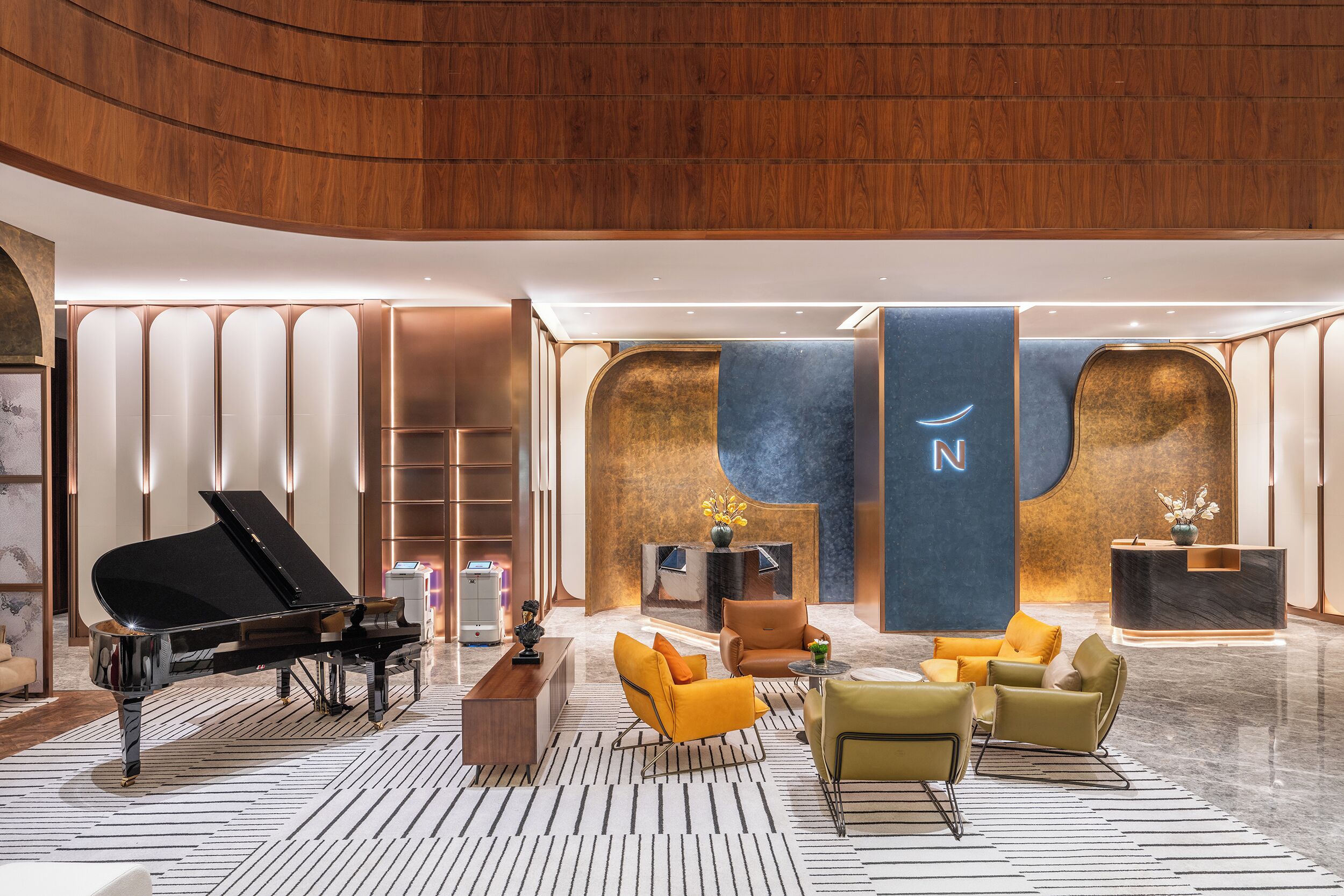 Een moderne lobby met een vleugelpiano, zachte zitplaatsen, een receptiebalie en een opvallende muur met een grote 'N'.