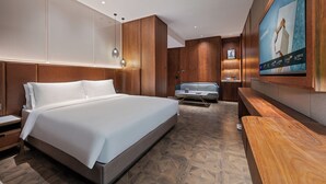 Una habitación de hotel moderna con una cama grande, paneles de madera, un área de descanso y un televisor.