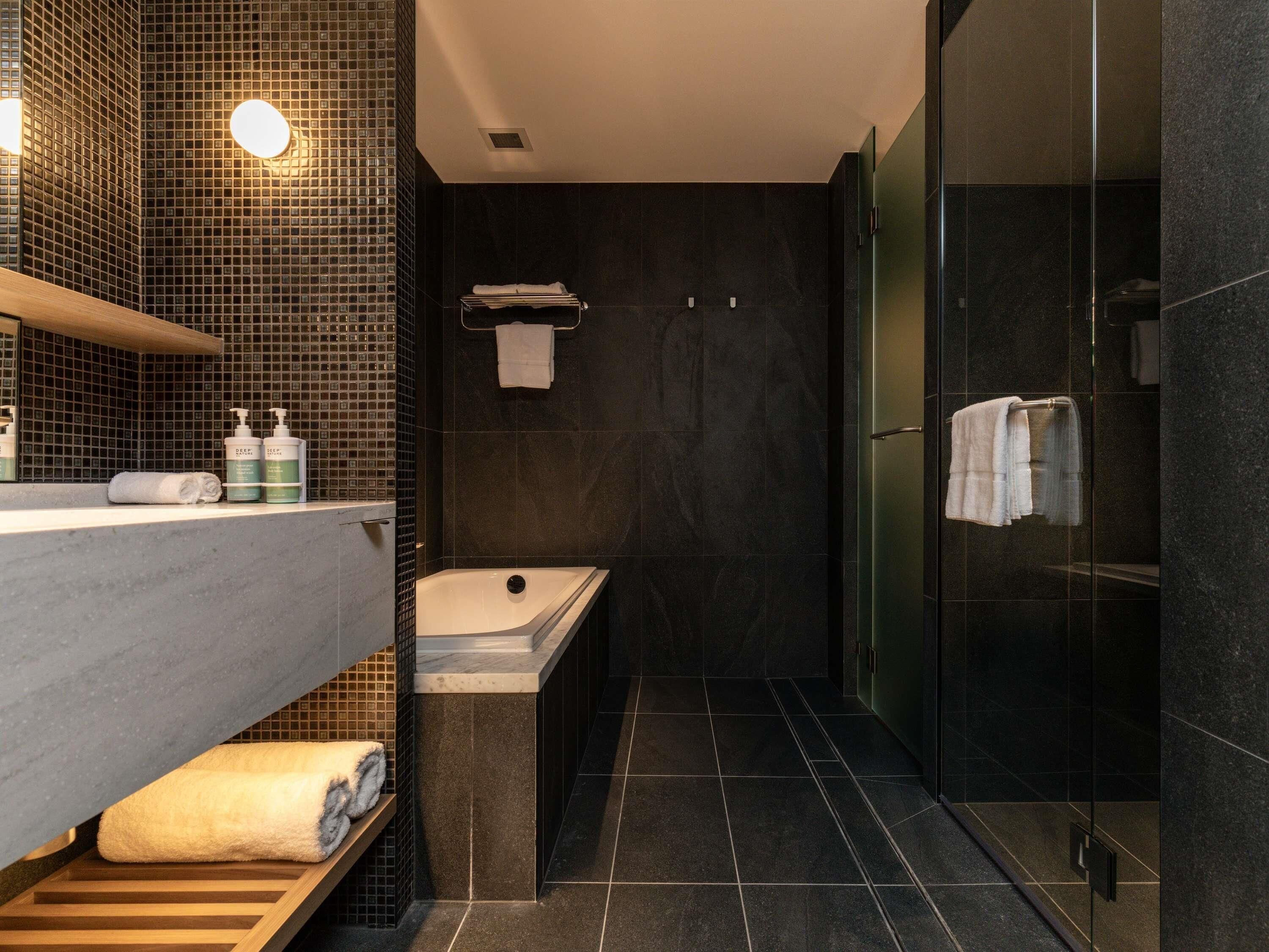 A modern bathroom with a bathtub, a glass-enclosed shower, and a vanity with a mirror and towel rack.
