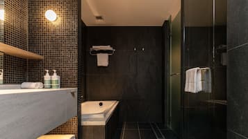 A modern bathroom with a bathtub, a glass-enclosed shower, and a vanity with a mirror and towel rack.