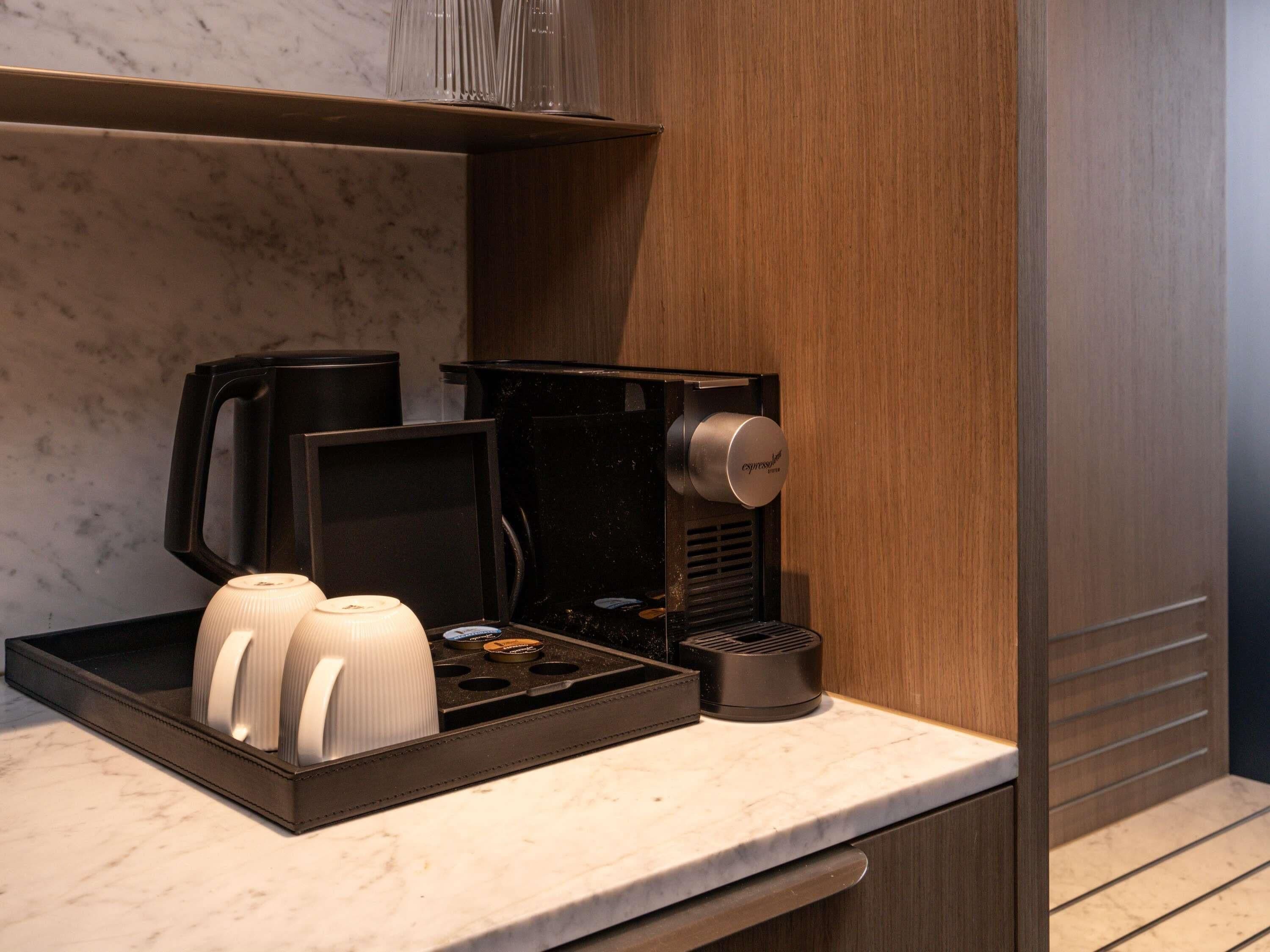 A coffee machine with a drip tray, a coffee pot, and a milk frother on a marble countertop.