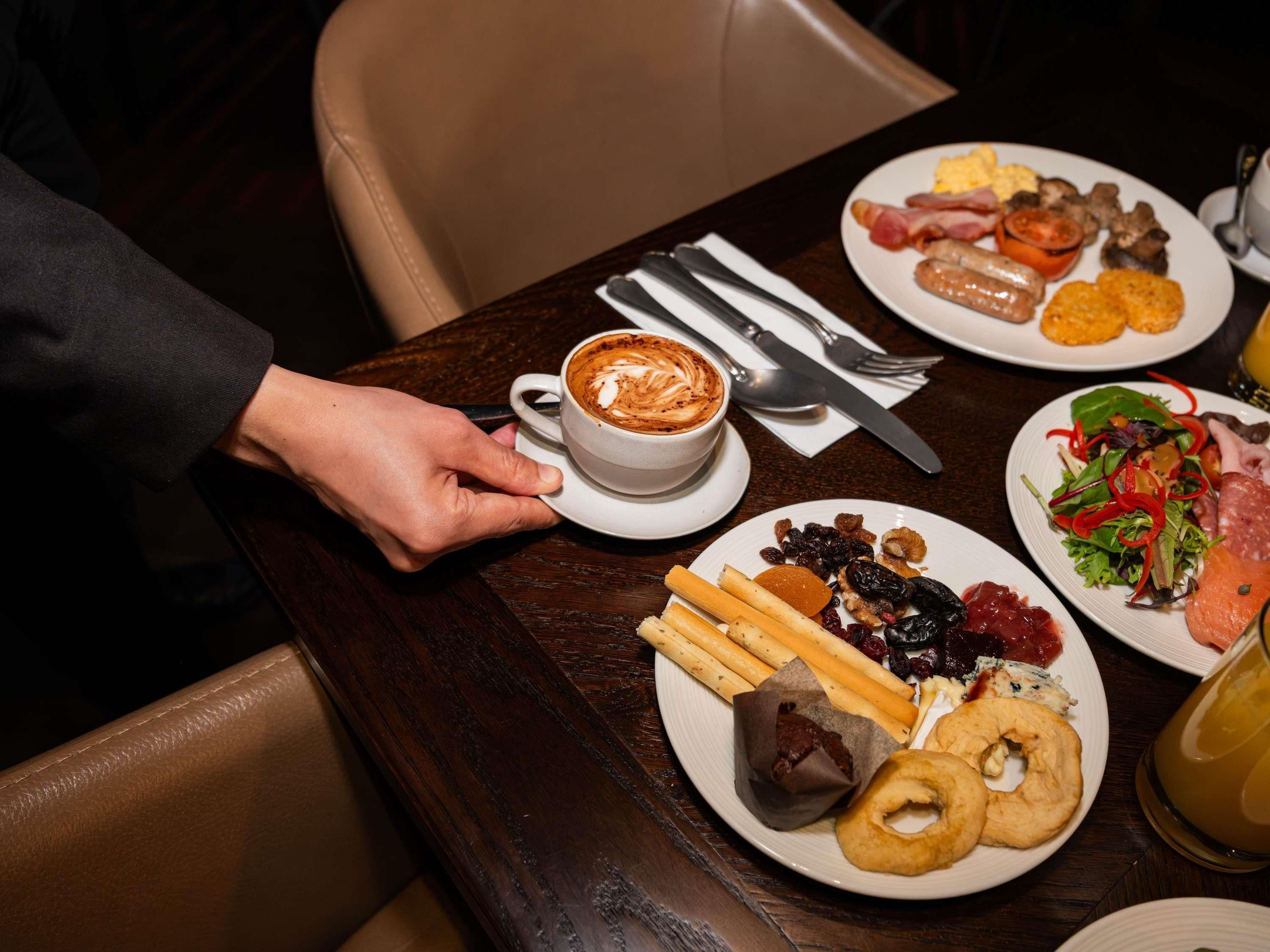 A dining table with plates of food, a cup of coffee, and cutlery.