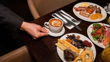 A dining table with plates of food, a cup of coffee, and cutlery.