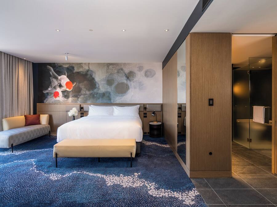 Habitación de hotel moderna con una cama grande, un sofá, un mural decorativo y vistas al exterior.