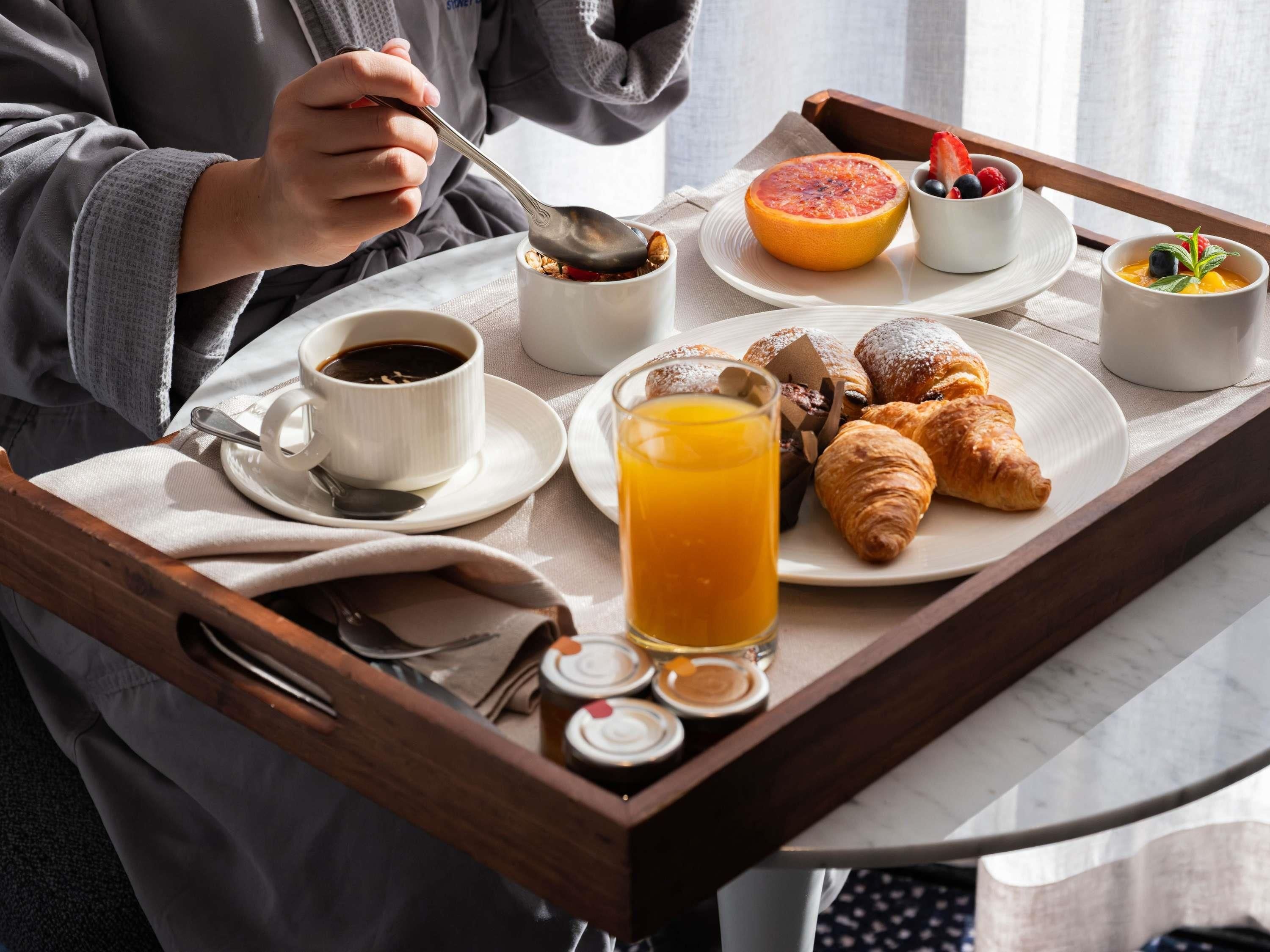 Bandeja de desayuno con cruasanes, pomelo, bayas, un vaso de zumo de naranja y una taza de café.
