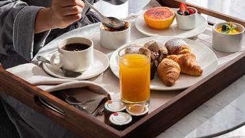 Bandeja de desayuno con cruasanes, pomelo, bayas, un vaso de zumo de naranja y una taza de café.