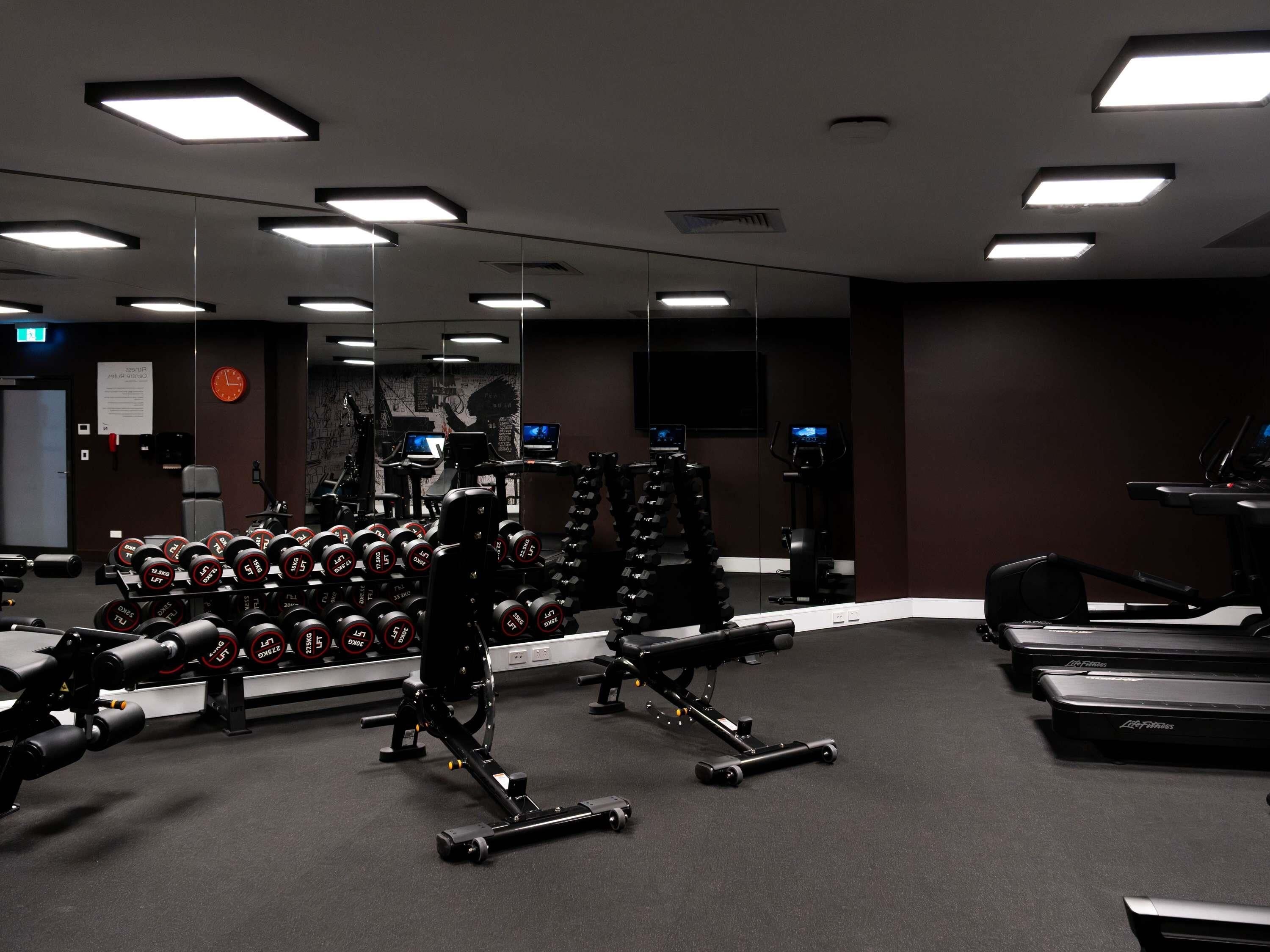 Ein Fitnessstudio mit Gewichte, Laufbändern und einer Spiegelwand.