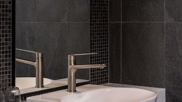 A bathroom with a white sink, a modern faucet, and a mirror with a black tiled backsplash.