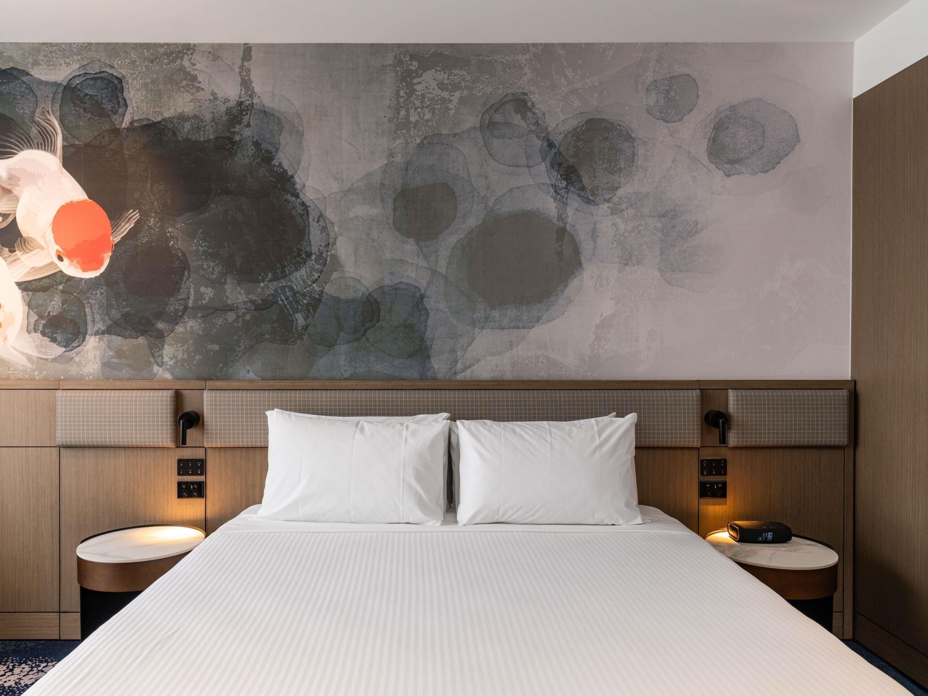Ein modernes Hotelzimmer mit einem großen Bett, zwei Nachttischen, einer Wand mit abstrakter Kunst und einem Holzkopfteil.