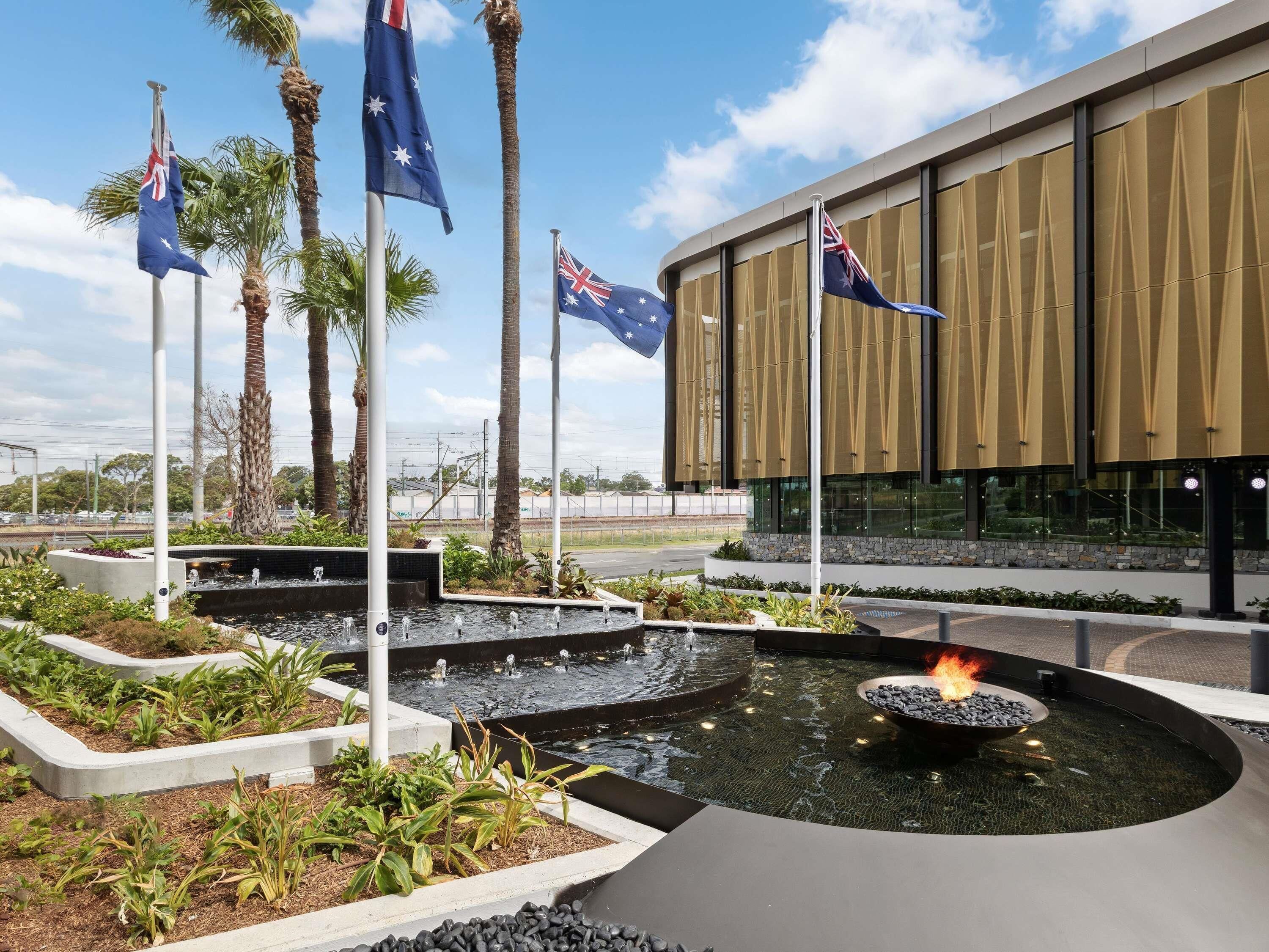 Een modern gebouw met Australische vlaggen, een waterpartij met vuurkorf en aangelegde tuinen.