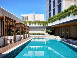 A modern outdoor swimming pool with a wooden deck, surrounded by buildings with brick facades and greenery. - Novotel Sydney Cabramatta (Canley Vale)