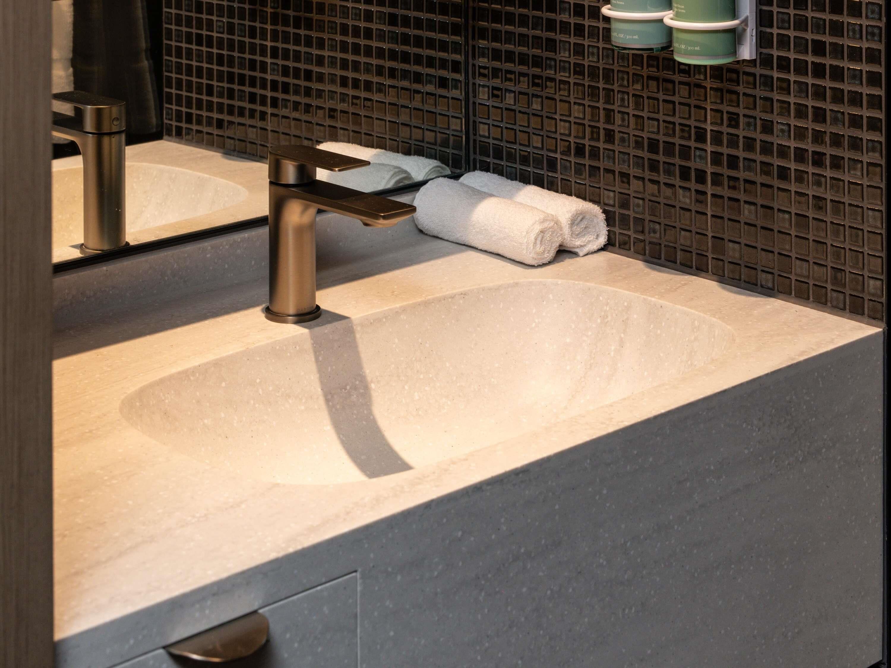 Une salle de bain avec un lavabo moderne, un robinet, un porte-serviettes avec des serviettes et un miroir.
