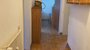 Un couloir doté d’un plancher en bois, d’un tapis à motifs, d’un radiateur et d’une armoire en bois sur laquelle est accroché un sac.