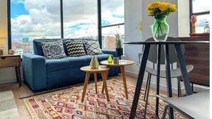 A modern living room with a blue sofa, a small round table, and a view of the city through large windows. - Beautiful Loft in Bogota-Charming View-Gym (Bogotá)