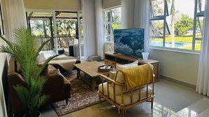 Un salon spacieux doté d’un grand téléviseur, de sièges confortables, d’une table basse et offrant une vue sur une piscine.