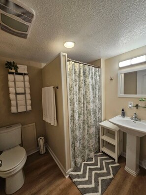 A bathroom with a shower curtain, toilet, sink, and towel rack.
