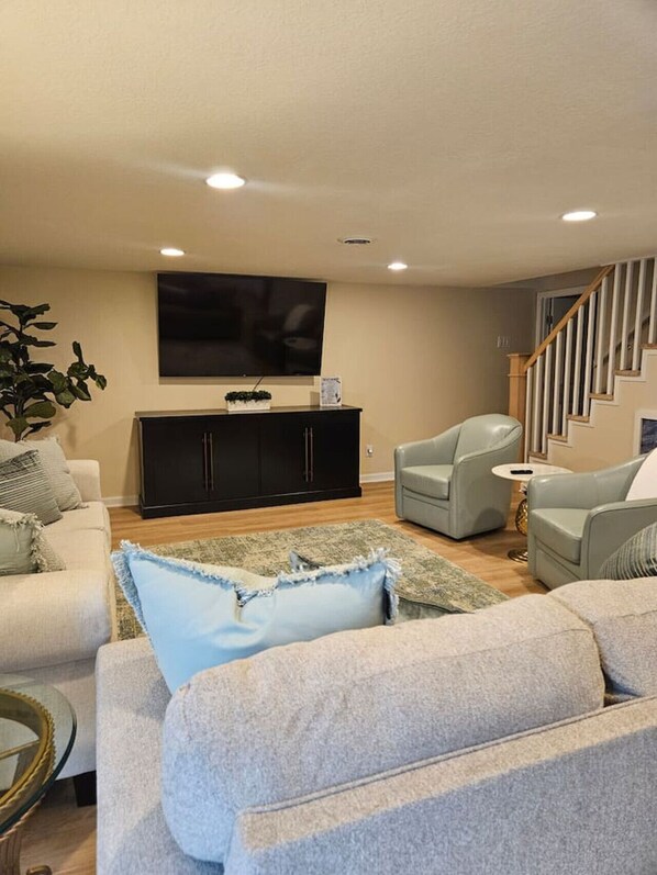 A living room with a sofa set, a television, a cabinet, and a staircase.