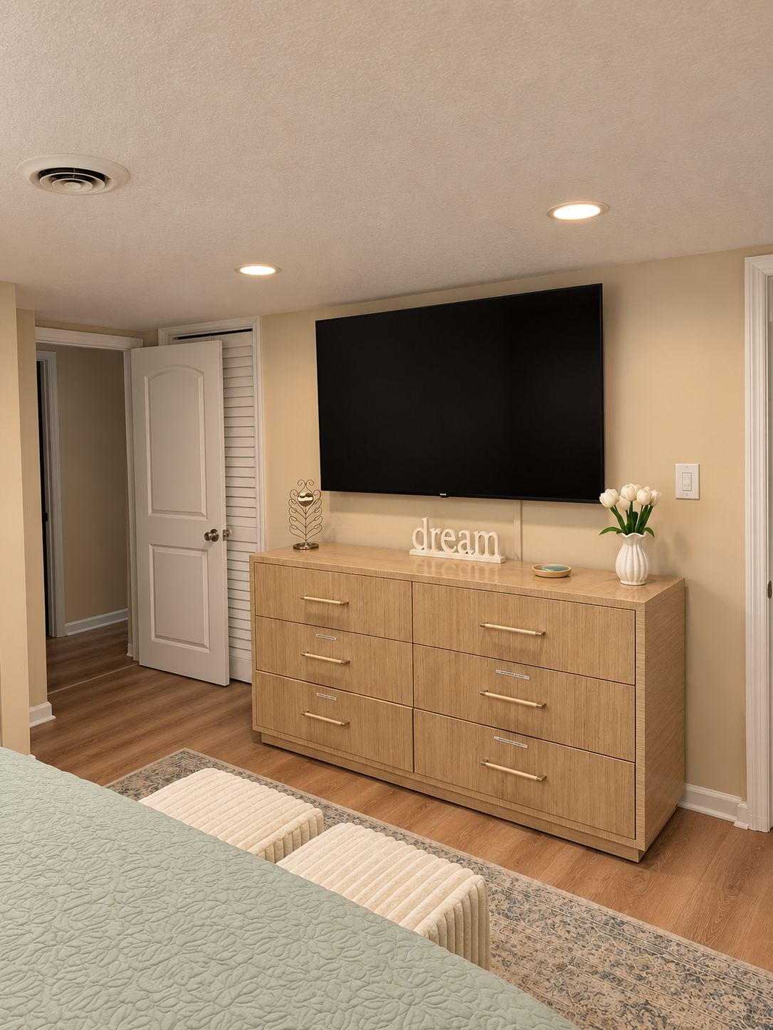 Une chambre à coucher avec un lit, une commode, un téléviseur à écran plat et une porte.