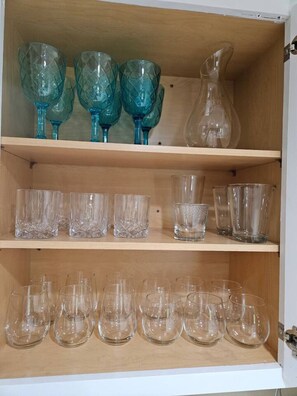 A wooden cabinet with shelves holding various glassware, including clear and blue glass cups and a pitcher.