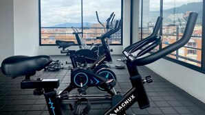 Et fitnessrum med træningsmaskiner og et stort vindue med udsigt over byen.