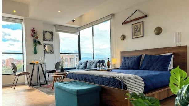 Et moderne soveværelse med en stor seng, et lille bord med stole, et vindue med udsigt og en balkon.
