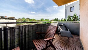 A rooftop terrace with wooden flooring, a black metal fence, and a modern building in the background.