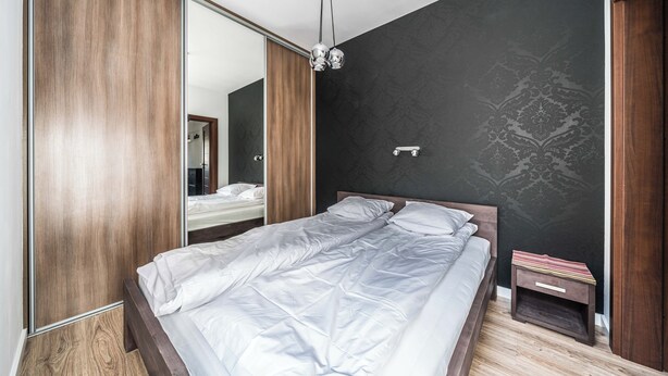 A bedroom with a bed, a wooden wardrobe, a nightstand, and a mirror.