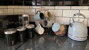 A kitchen counter with labeled containers for tea, coffee, and sugar, a kettle, and various mugs. - Buccleuch Whole Apartment (Kettering)