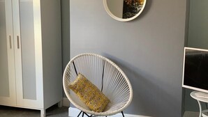 A room with a white rattan chair with a patterned cushion, a round mirror on the wall, and a television on a small table. - Buccleuch Whole Apartment (Kettering)