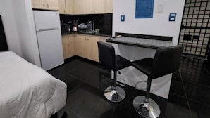 A compact kitchen with modern appliances, a small dining area with two bar stools, and a white bed. - Suite in San Miguel Steps from Monagas Plaza (Monagas)