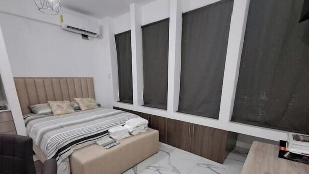 Een moderne slaapkamer met een bed, nachtkastje, stoel en een raam met gordijnen.