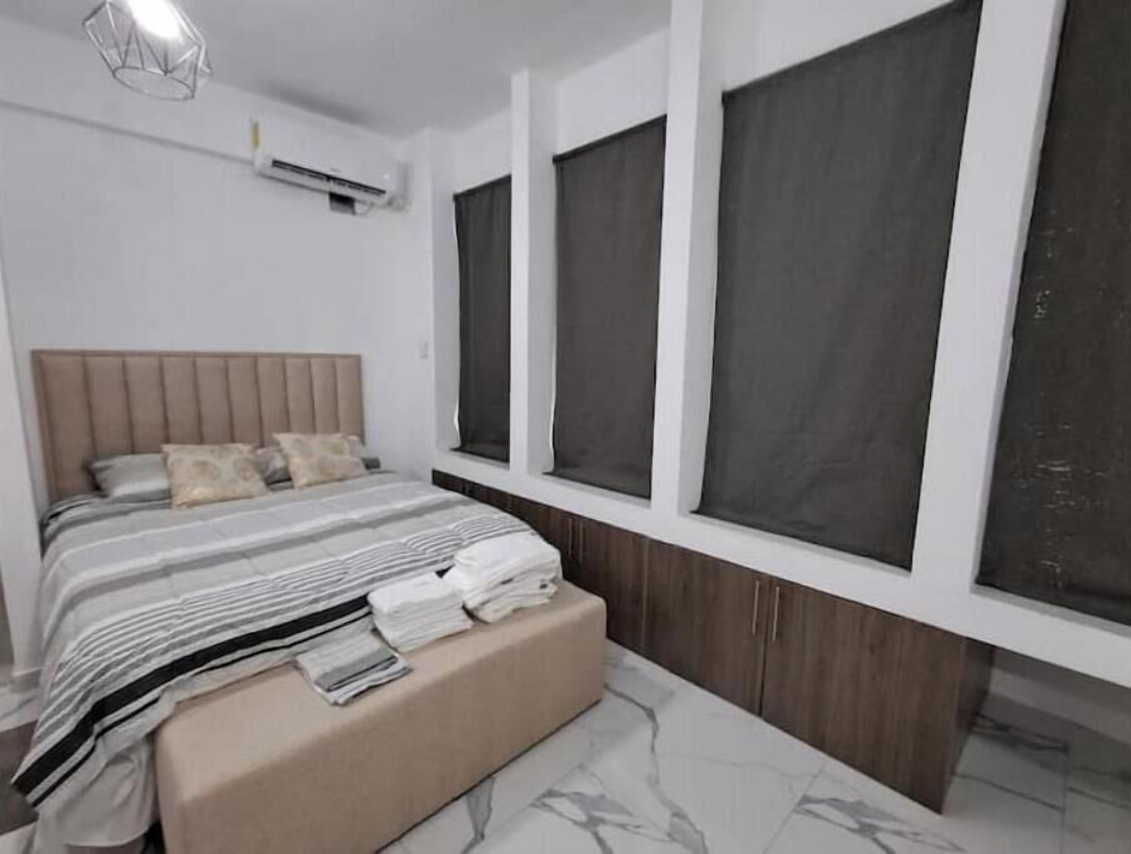 Een moderne slaapkamer met een groot bed, een nachtkastje, een bankje met handdoeken en een raam met uitzicht.