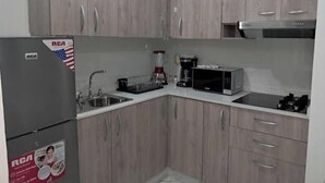 Een kleine keuken met houten kastjes, een roestvrijstalen spoelbak, een koelkast, een magnetron en een koffiezetapparaat.