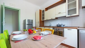 Une cuisine moderne avec des meubles blancs, un plan de travail en bois et une table à manger dressée avec des assiettes, des couverts et des fruits.