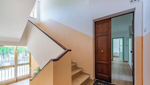 Un escalier avec une rampe en bois menant à une porte sur laquelle est posé un paillasson avec l’inscription « BIENVENUE ».