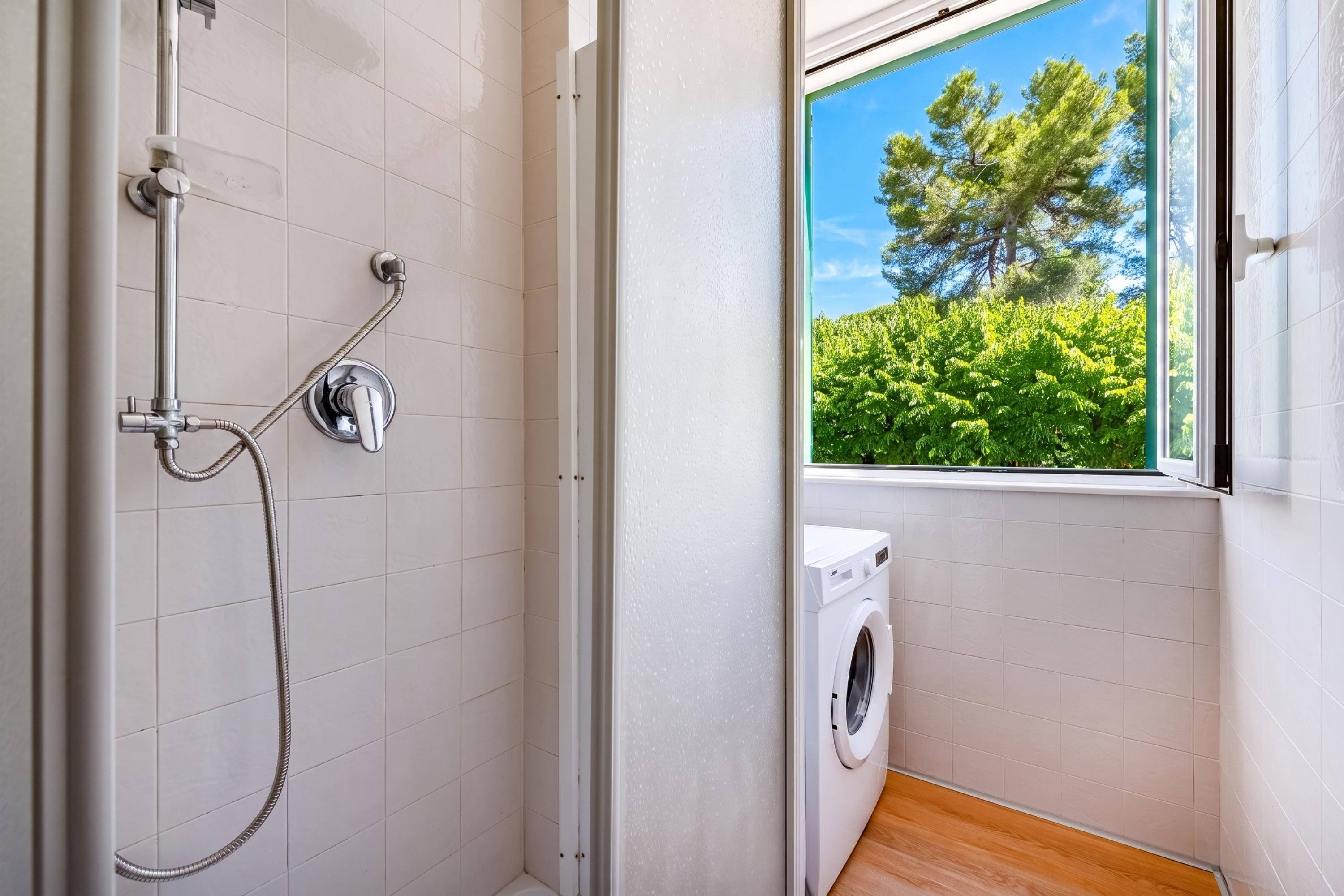 Une salle de bain avec douche, un lave-linge et une fenêtre donnant sur un espace verdoyant.