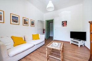 Una sala de estar con un sofá blanco, un televisor y cuadros en la pared.