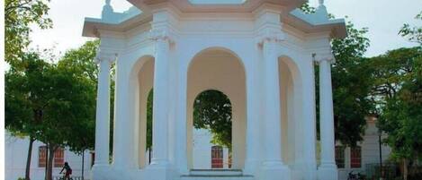 A white gazebo with a central archway and steps leading up to it, surrounded by trees.