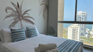 A bedroom with a large bed, striped pillows, and a view of tall buildings through a window.