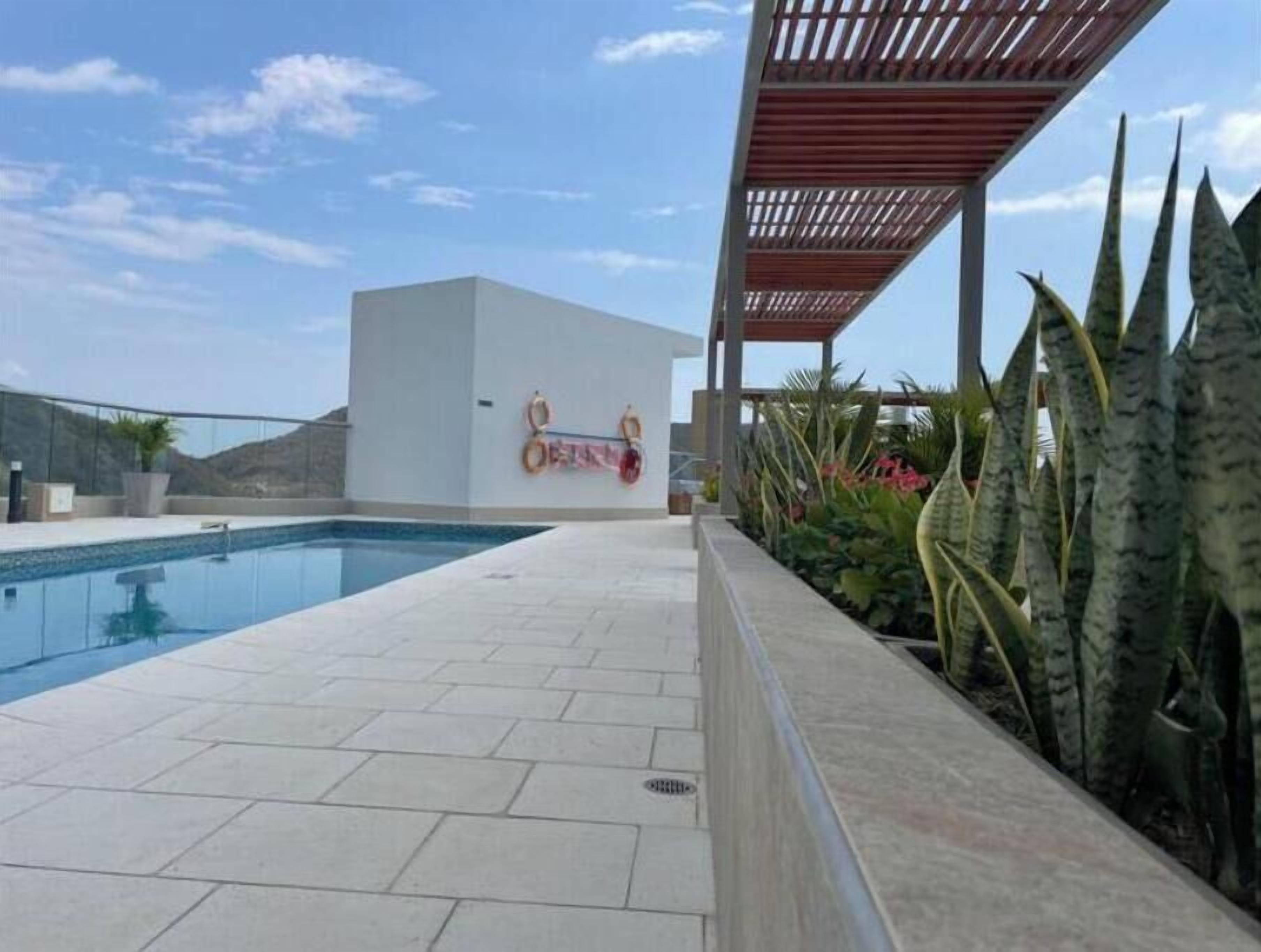 Une piscine avec une terrasse carrelée, un espace couvert doté d’un toit en bois et un mur muni d’un porte-serviettes.