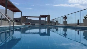 A clear blue swimming pool with a covered area, potted plants, and a view of distant hills.