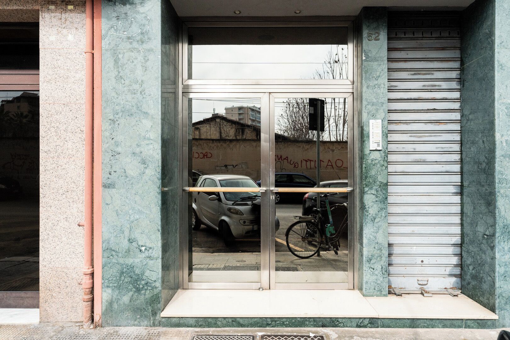 Entrada de un edificio con puerta de vidrio, reja de metal y una bicicleta estacionada en el interior.