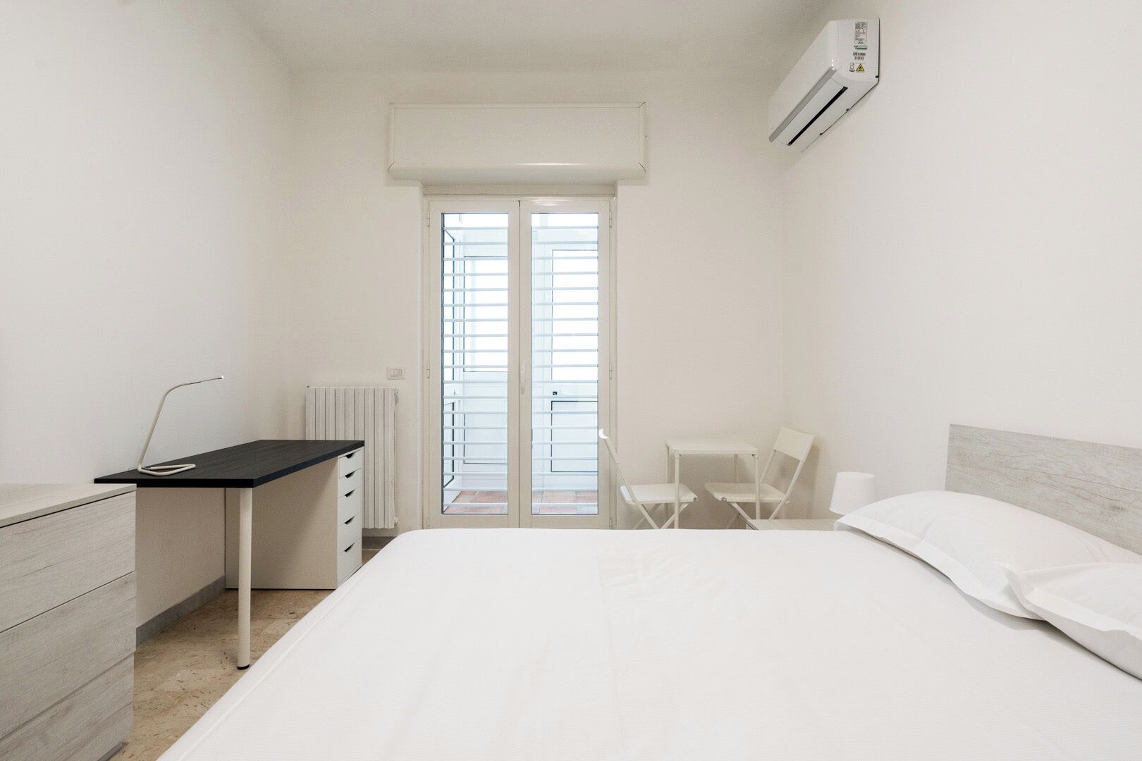 A minimalist bedroom with a bed, a desk, and a chair.