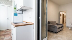 Une cuisine moderne équipée d’une cuisinière intégrée et d’une porte-fenêtre coulissante donnant sur un espace de vie comprenant un canapé et un fauteuil.
