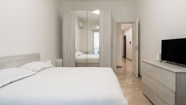 Une chambre à coucher avec un lit, une commode, une télévision et un miroir.