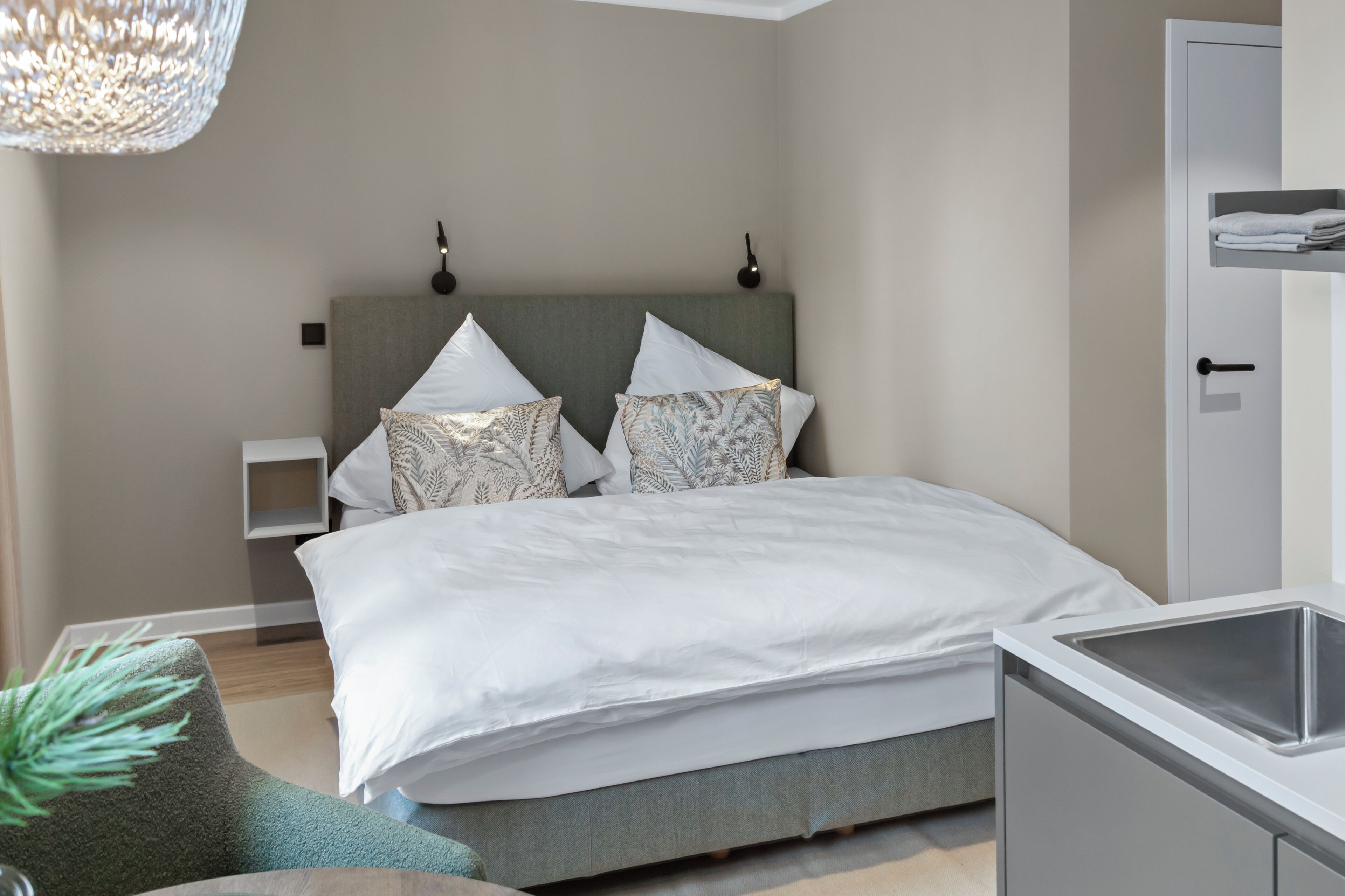 Ein modernes Schlafzimmer mit Bett, Nachttischen, einer Pendelleuchte und einem fest installierten Waschbecken.