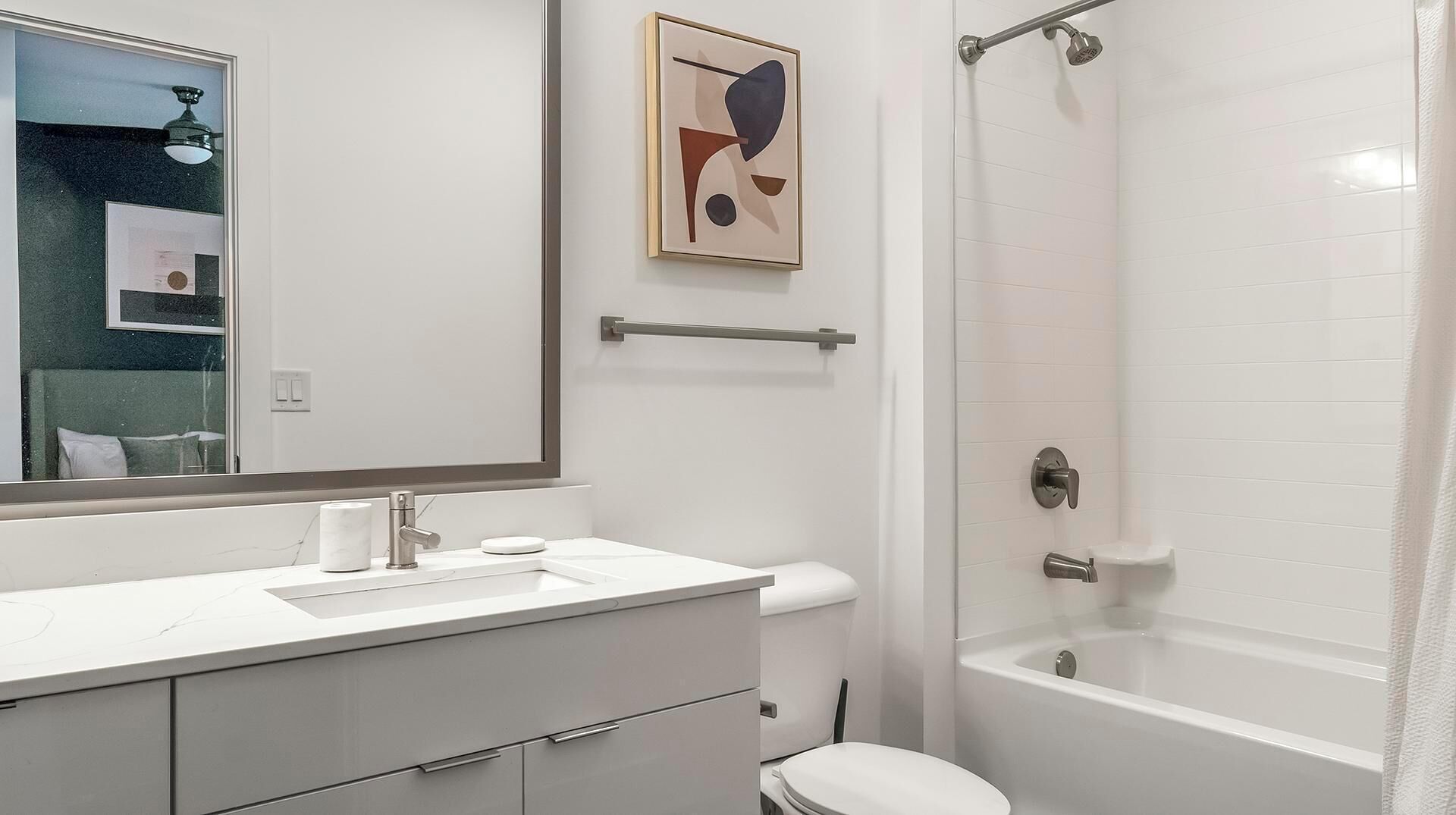A modern bathroom with a white vanity, a toilet, a bathtub, and a shower.